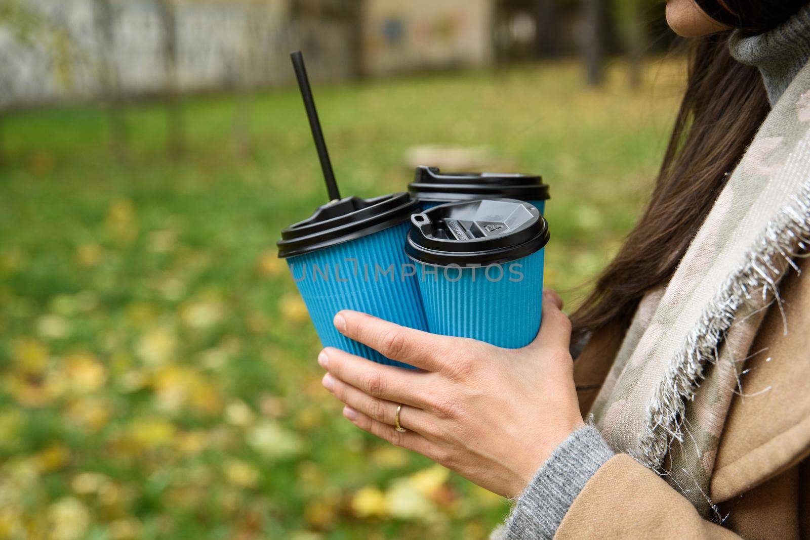 Close-up a woman hands holding three blue paper cups of coffee on autumn nature background with colorful grass.