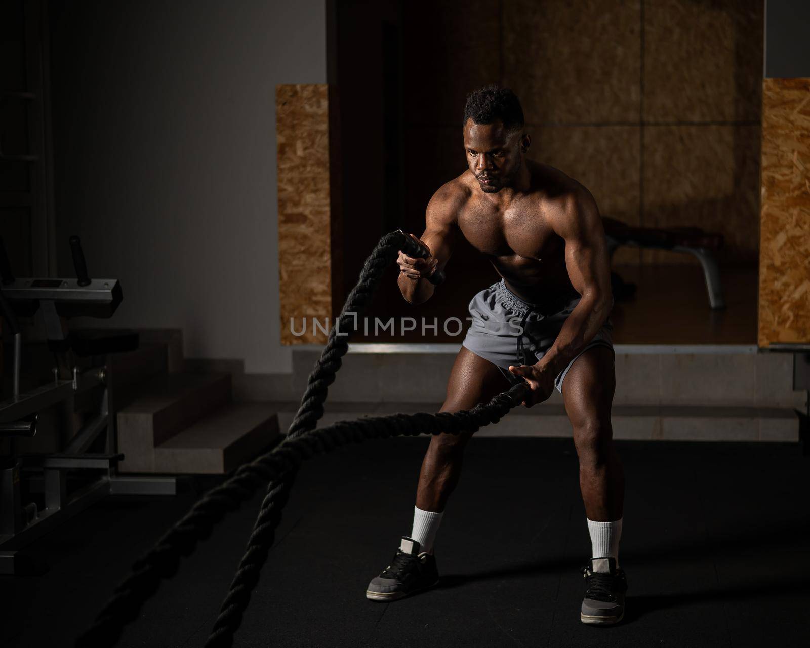 Attractive african american man with naked torso doing endurance exercises with trope