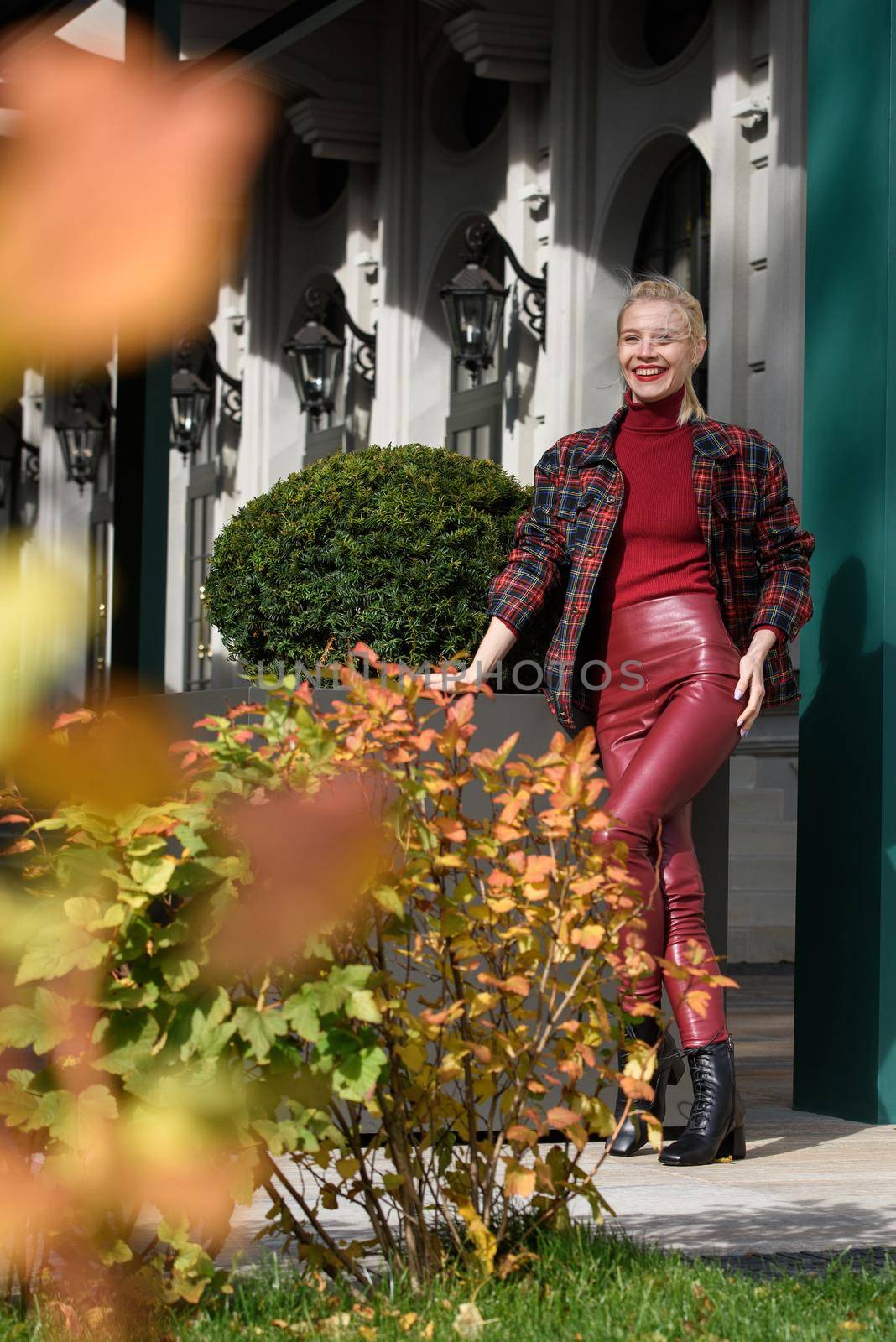 A beautiful, modern, fashionable blonde girl with a red lipstick posing outdoors . red leather leggings, turtleneck and checkered jacket. fit figure. by Ashtray25