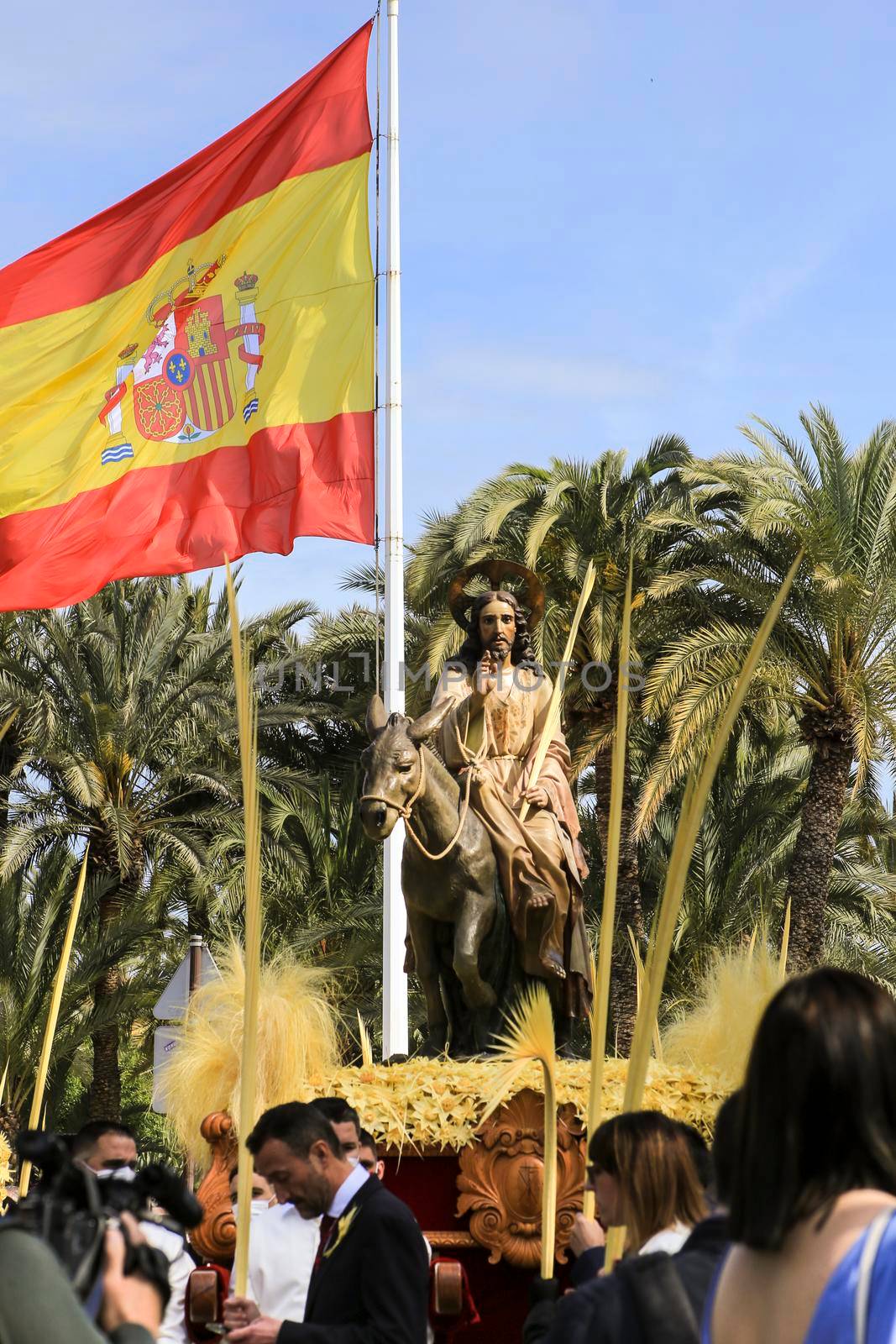 Elche, Alicante, Spain- April 10, 2022: Jesus Christ next to the Spanish flag at the traditional procession of white palms on the Palm Sunday of Elche