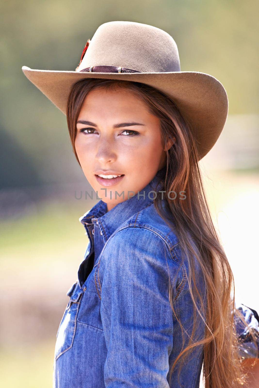 Portrait of an attractive young cowgirl standing in the sun.