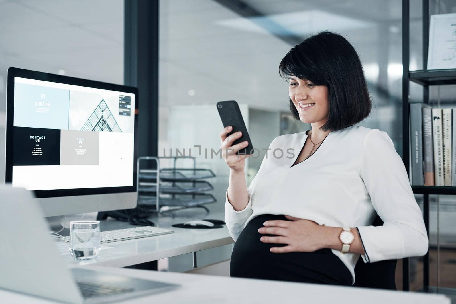 Checking my emails couldnt be easier. Cropped shot of an attractive pregnant businesswoman sitting alone in the office and using her cellphone. by YuriArcurs