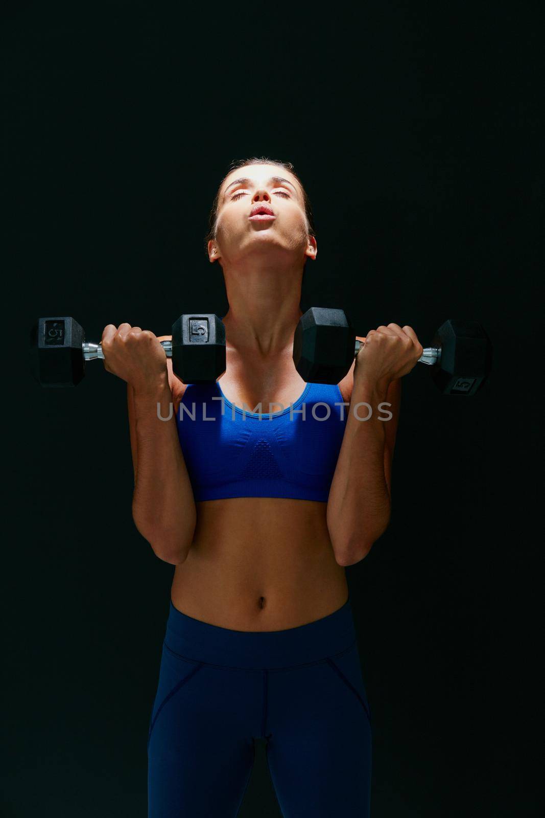 Hustle for your muscle. Studio shot of a fit young woman working out with weights against a dark background. by YuriArcurs