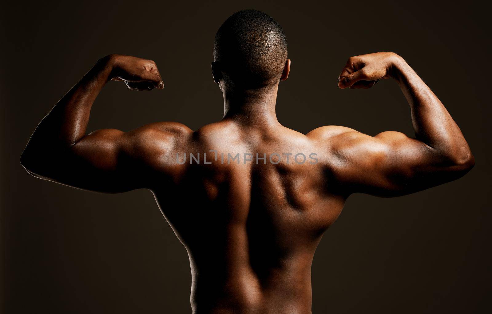 Rearview studio shot of a fit young man flexing against a black background.