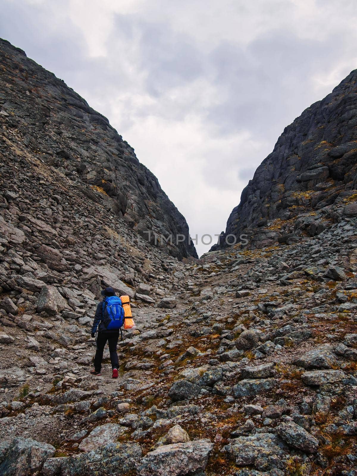 A young woman tourist with a backpack goes through a lifeless rocky pass.