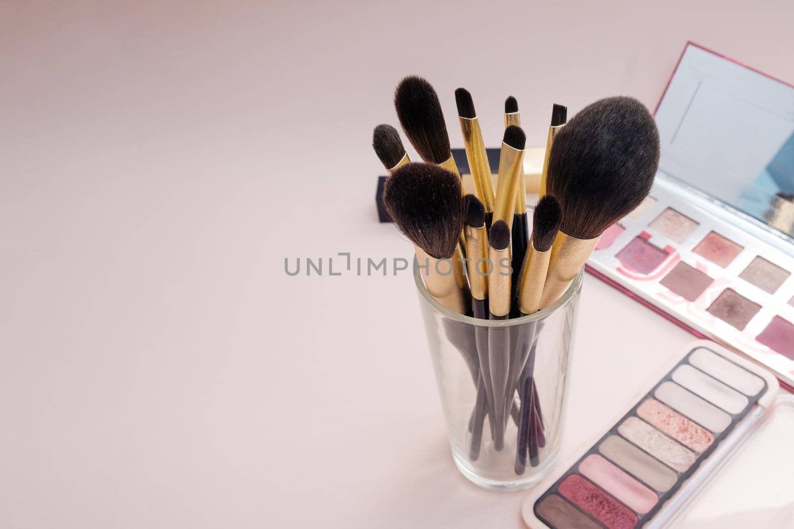 Composition with decorative makeup products golden brushes and colorful eye shadows on pastel pink background. photo