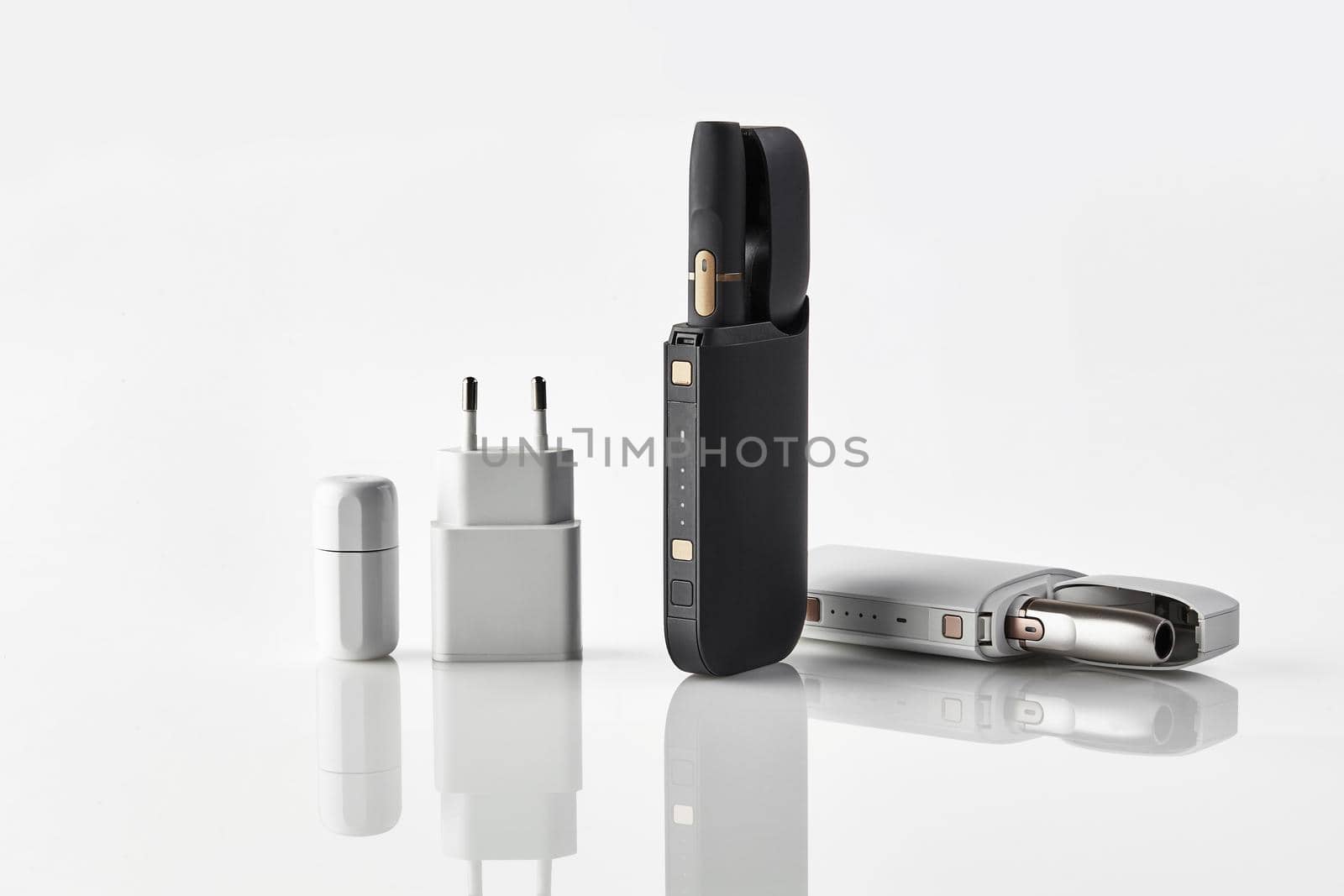 New generation black and white electronic cigarettes in open batteries, cleaner, power adapter isolated on white. Hi-tech heating tobacco system. Tools used to help stop smoking. Close up, copy space