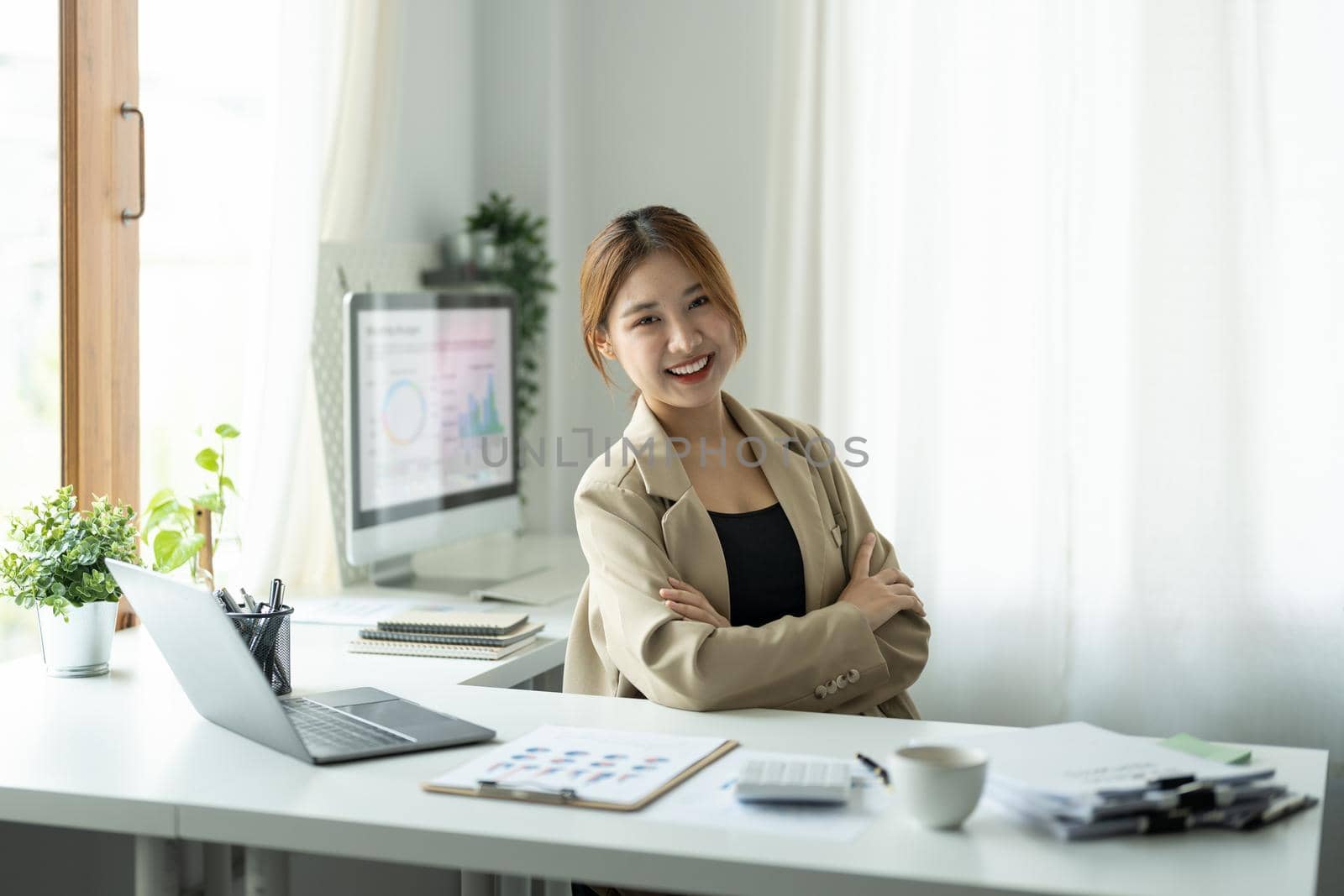 Portrait of young beautiful asian businesswoman looking at camera and smile, arms crossed in modern office workplace.