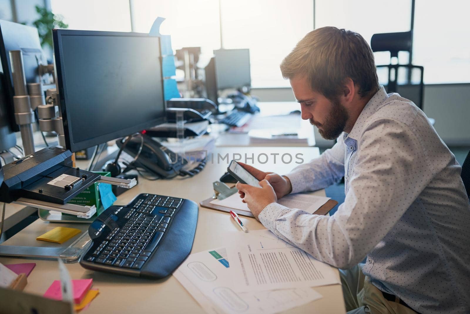 Reading an important message. Shot of a focused young businessman texting on his cellphone while being seated behind his desk in the office. by YuriArcurs