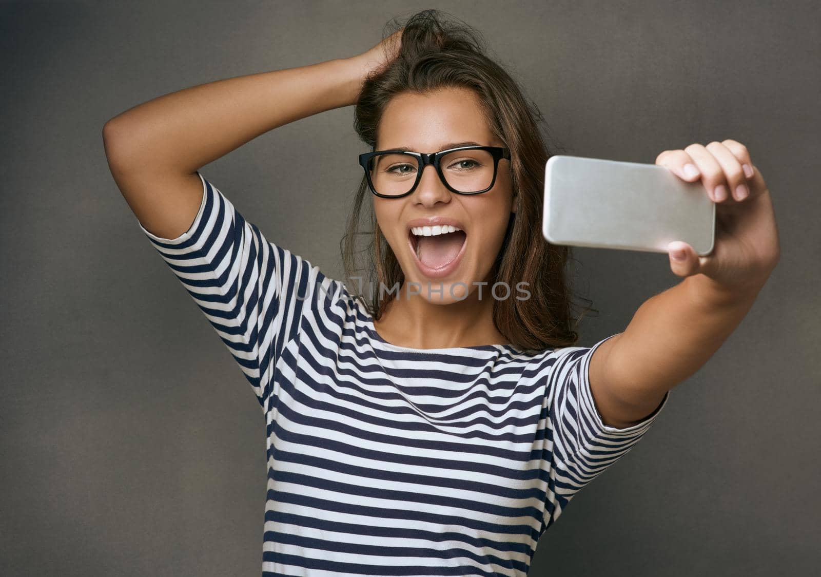 Studio shot of an attractive young woman taking a selfie against a grey background.