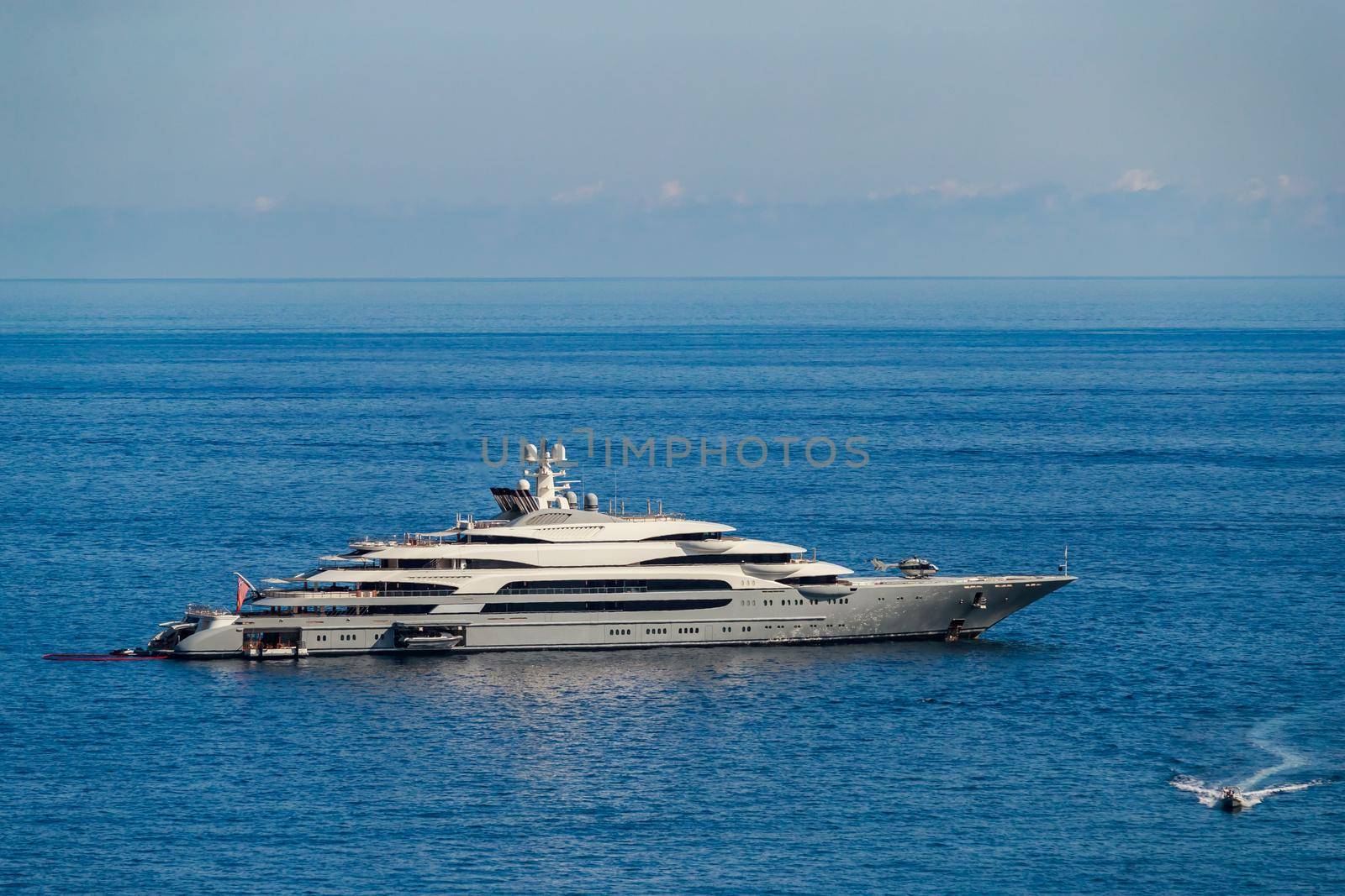 The huge mega yacht is moored in sea off the coast of the azur coastline at sunny day, the chrome plated handrail, sun reflection on glossy board of the motor boat. High quality photo