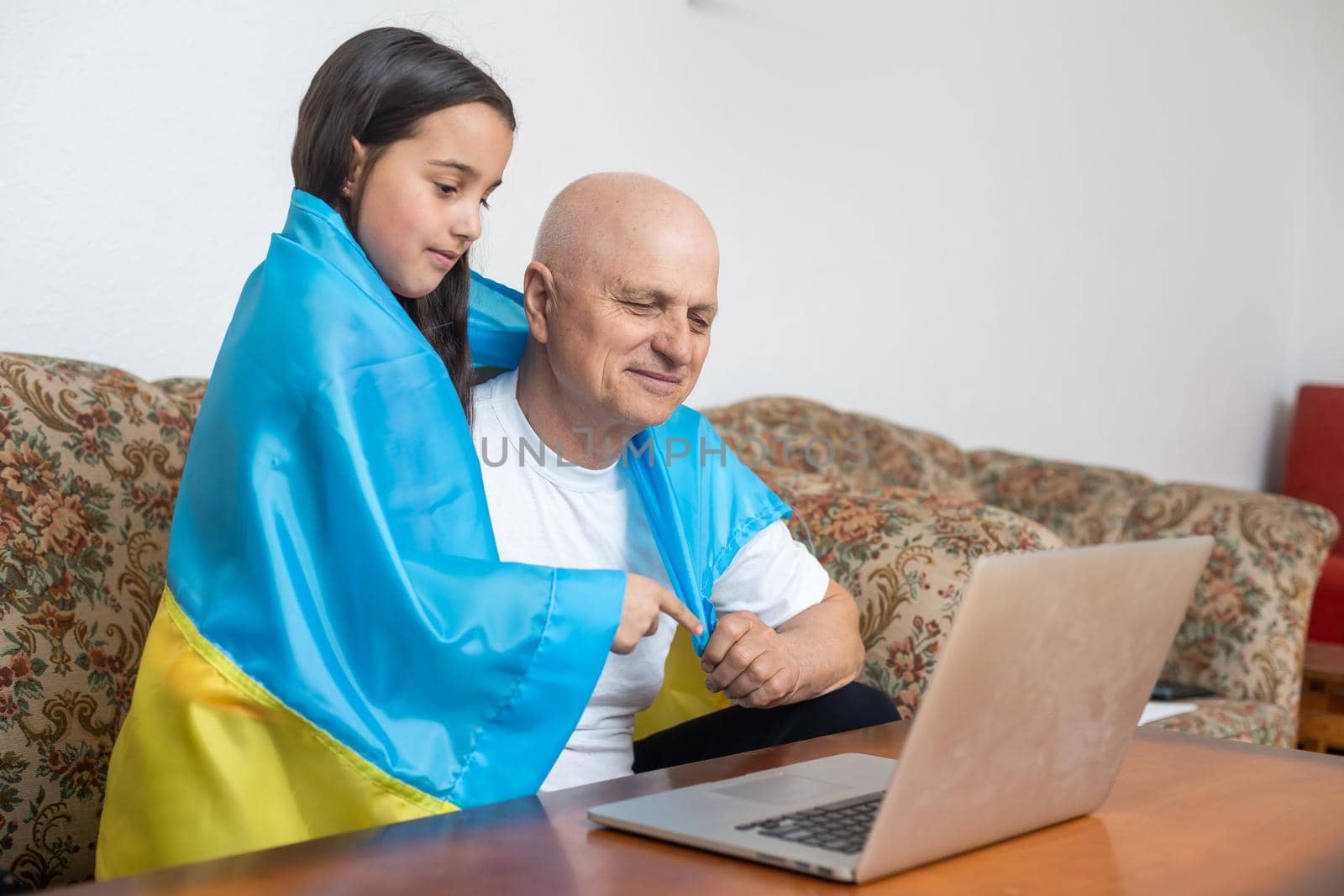 Grandfather and granddaughter with laptop and flag of Ukraine.