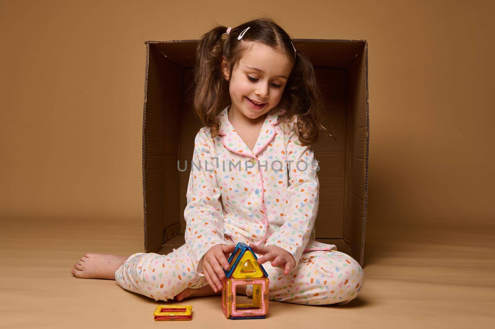 Beautiful Caucasian preschooler girl playing with lots of colorful plastic blocks constructor and building a cozy house. Fine motor skills development, kids entertainment and education concept by artgf