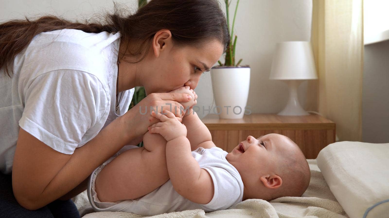 Authentic Young Caucasian Woman Holding Newborn Baby. Mom And Child On Bed. Close-up Portrait of Smiling Family With Infant On Hands. Happy Marriage Couple On Background. Childhood, Parenthood Concept by mytrykau