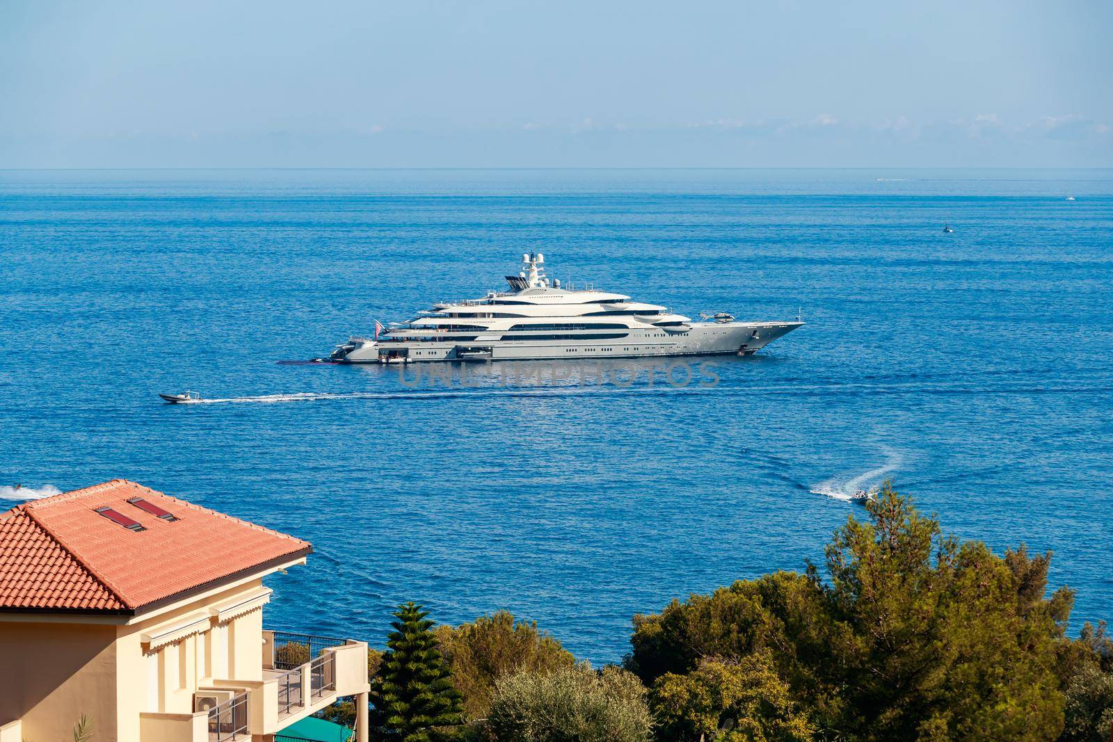 The huge mega yacht is moored in sea off the coast of the azur coastline at sunny day, the chrome plated handrail, sun reflection on glossy board of the motor boat. High quality photo