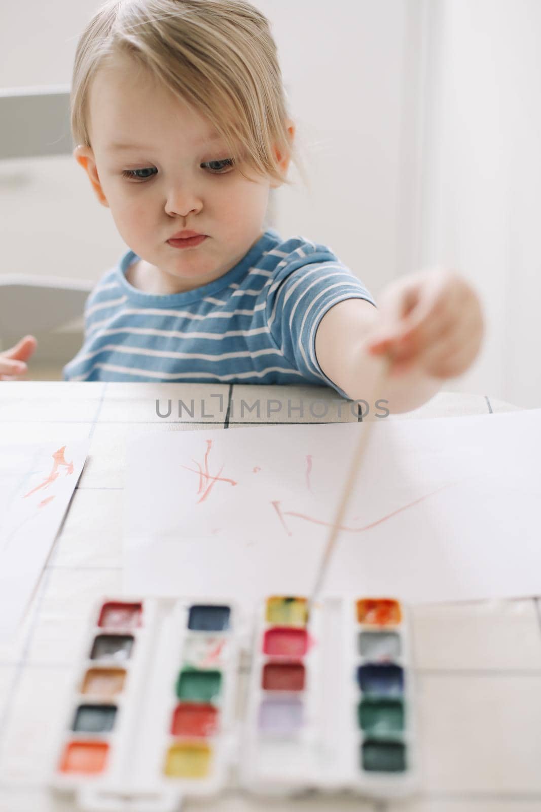 Child painting and drawing with watercolor paint at white table. Development of creative potential in children