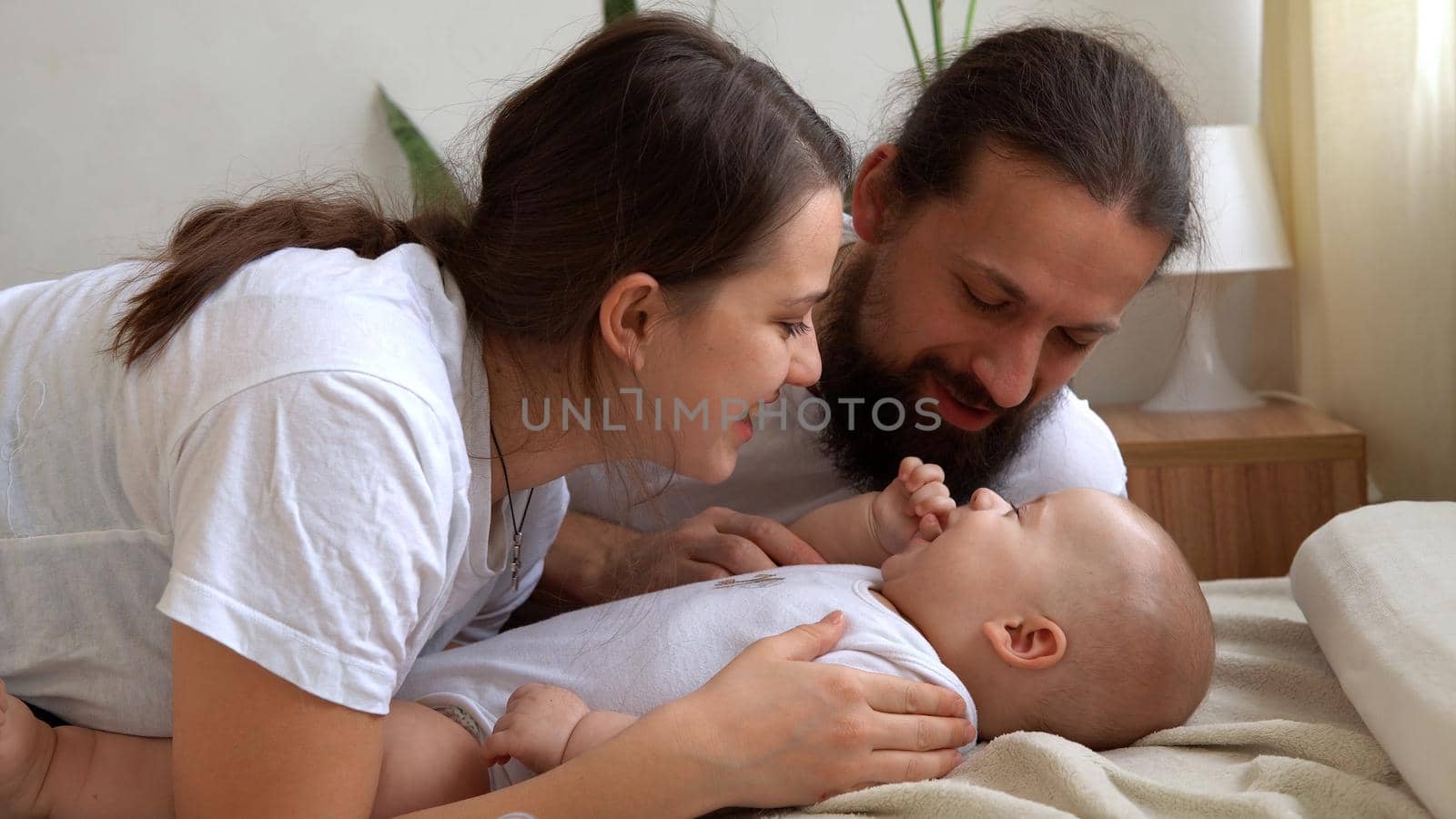 Woman And Man Holding Newborn. Mom, Dad And Baby On Bed. Close-up. Portrait of Young Smiling Family With Newborn On Hands. Happy Marriage Couple On Background. Childhood, Parenthood, Infants Concept.