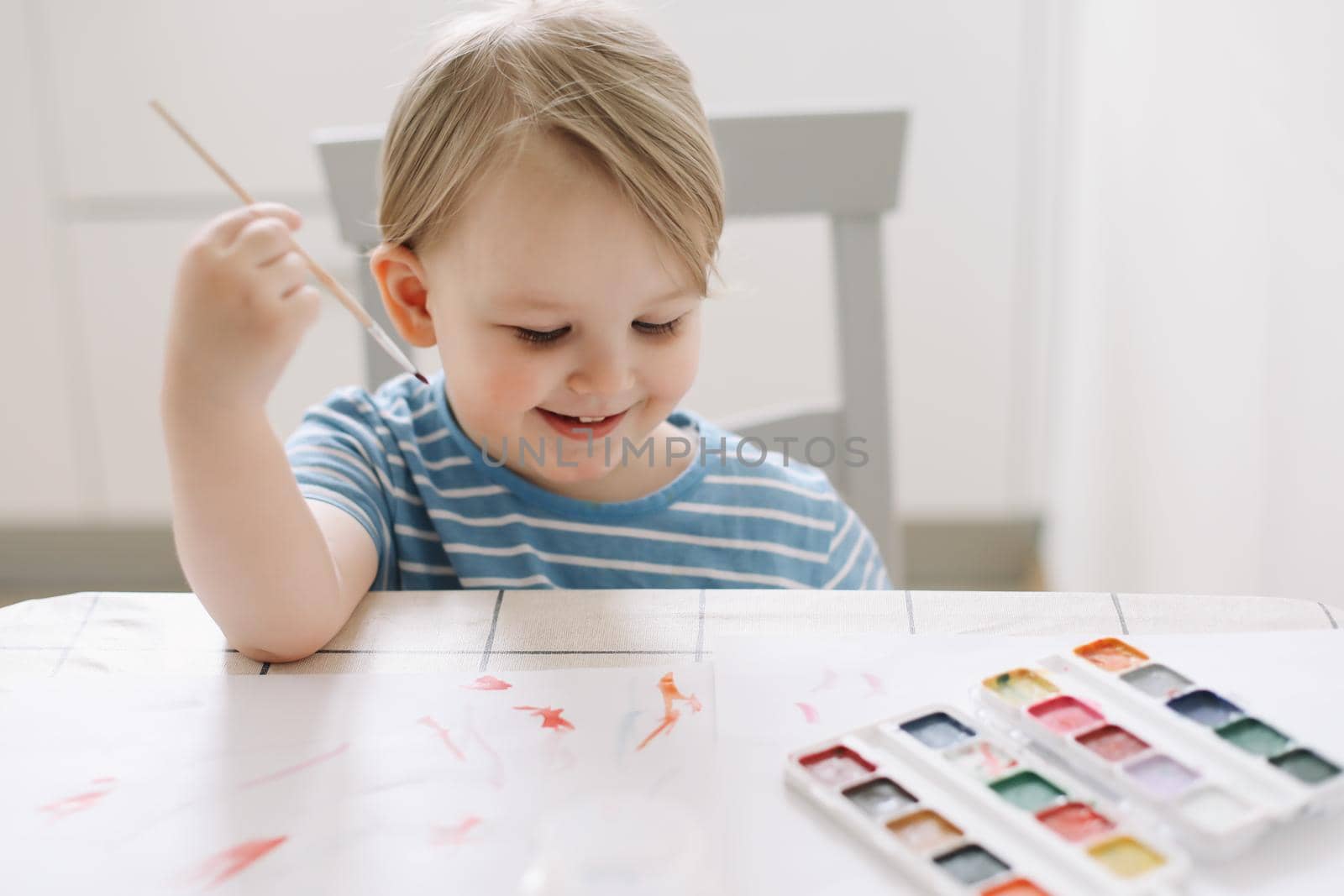 Child painting and drawing with watercolor paint at white table. Development of creative potential in children