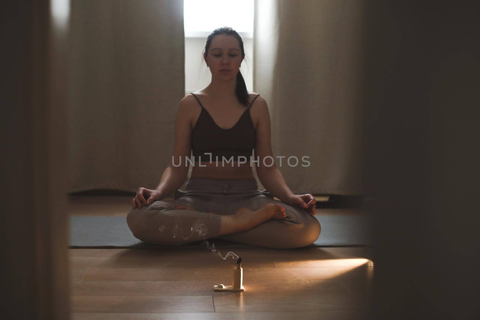 young woman doing yoga and practising meditation with a burning aroma stick in front of her. mental health concept.