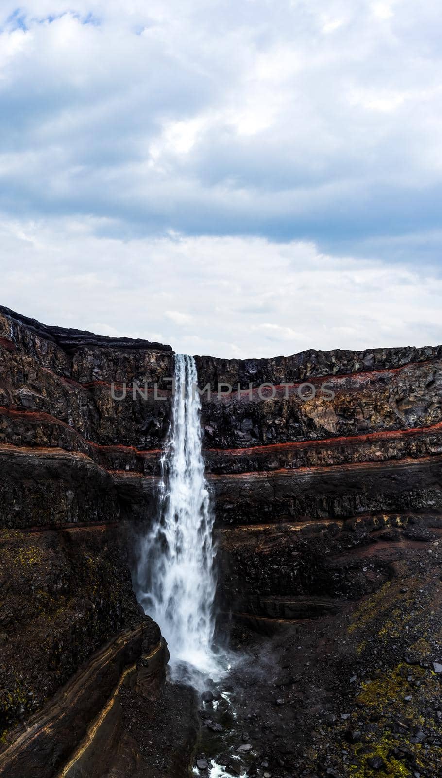 Hengifoss waterfall with deep red layers under cloudy sky by FerradalFCG