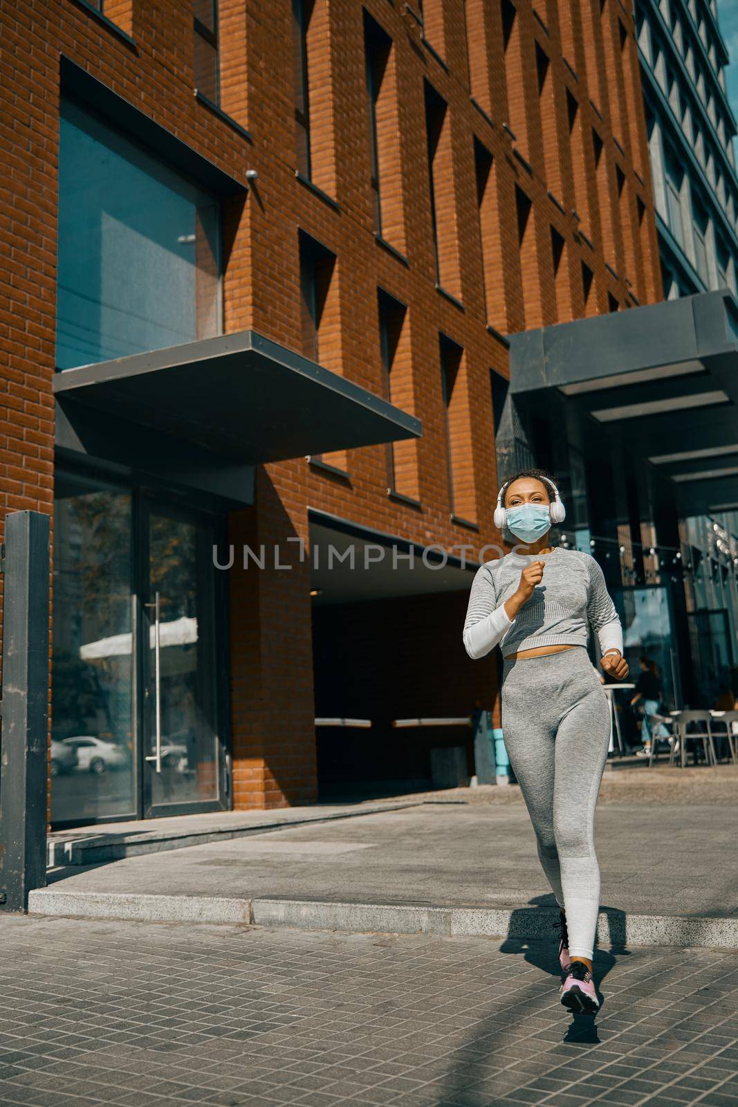 Woman in mask and headphones jogging during Covid 19 quarantine. Sports, coronavirus concept