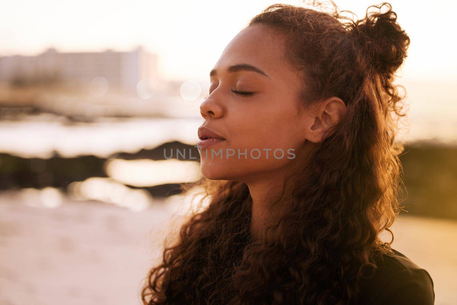 The universe speaks when you stop and listen. Shot of an attractive young woman sitting alone on a mat and meditating on the beach at sunset. by YuriArcurs