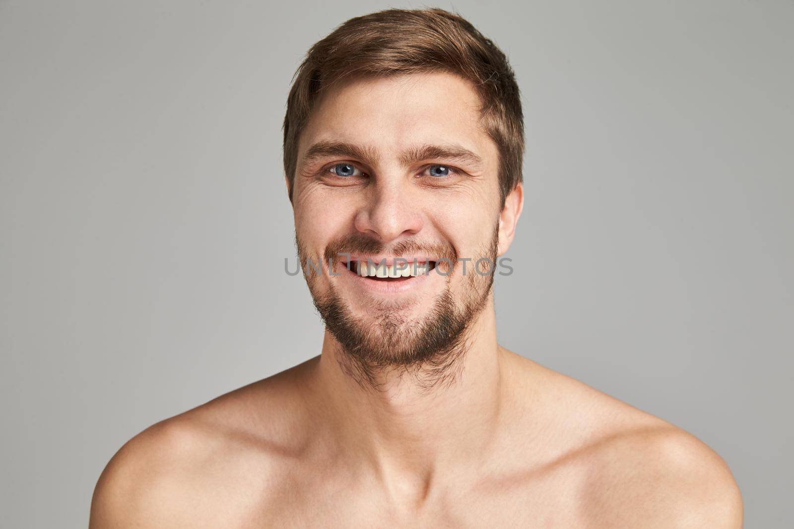 Portrait of a smiling young man with bare swimmers shoulders on a gray background, powerful, beard, charismatic, adult, brutal, athletic, edited photo, bright smile, white teeth smile, look in camera. High quality photo