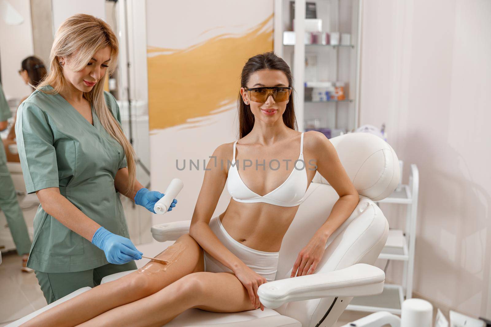 Cosmetologist applying ointment on woman legs before hair removal procedure in beauty salon by Yaroslav_astakhov