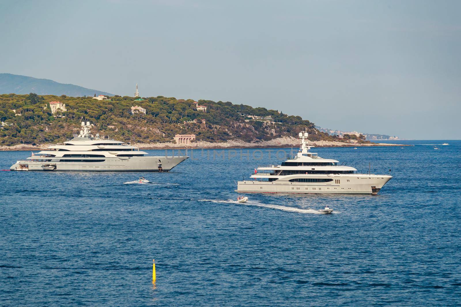 The two huge mega yachts are moored in sea at sunny day, the chrome plated handrail, sun reflection on glossy board of the motor boat. High quality photo