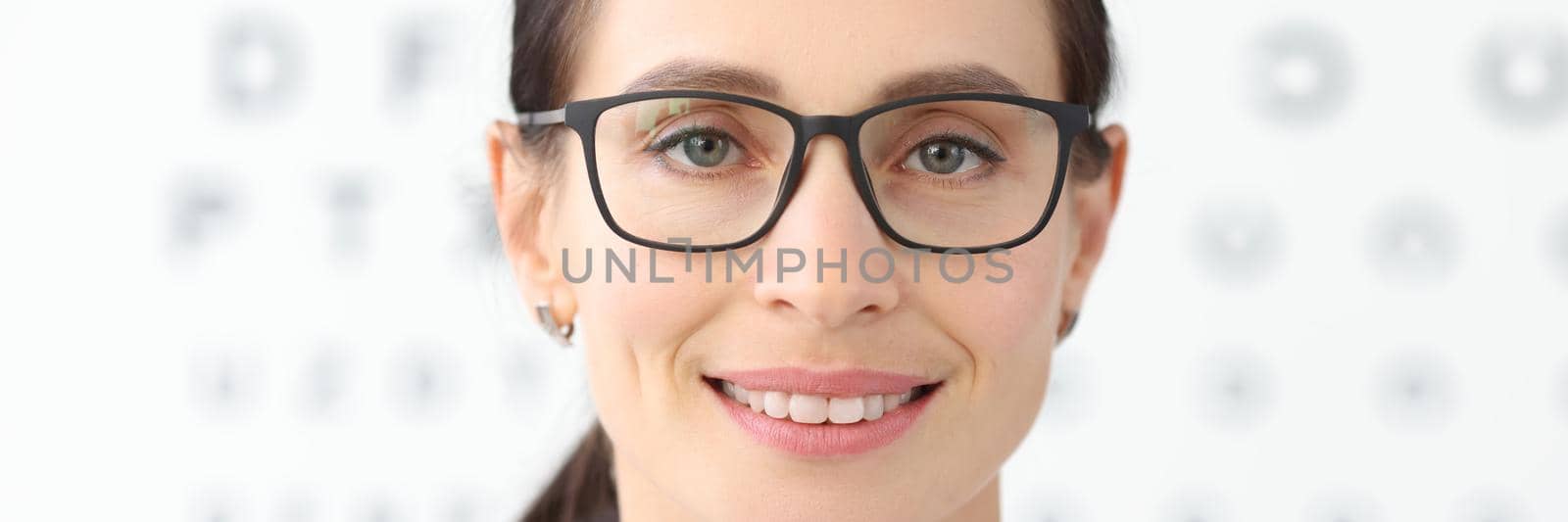 Woman ophthalmologist with glasses standing against background of table for eye test. Laser vision correction concept