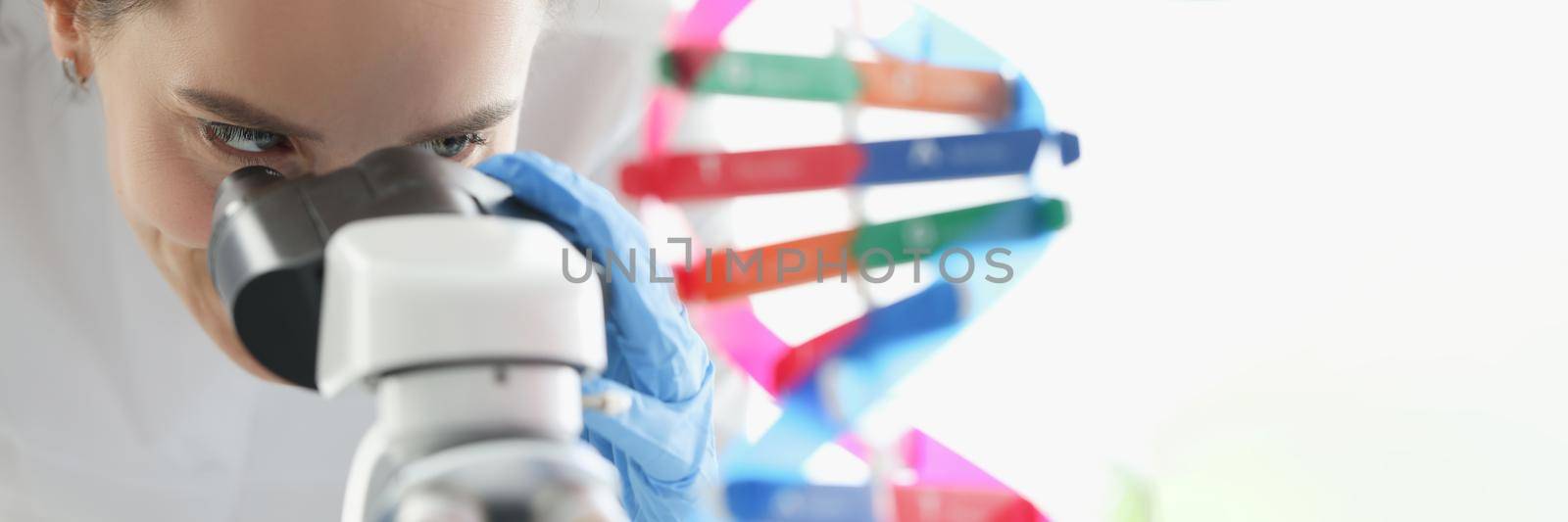 Woman scientist looking through microscope near dna molecule mockup in lab. Scientific genetic research concept