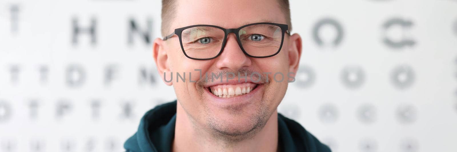 Portrait of smiling man with glasses on background of table for vision test. Correction of myopia selection of glasses concept