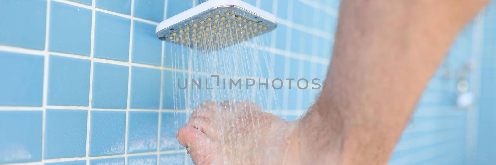 Man washing his feet from sand under shower on beach closeup. Foot hygiene concept