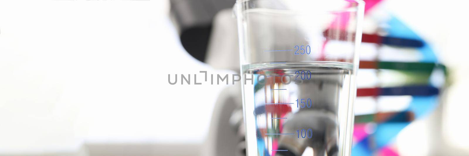 Glass of water standing near dna molecule mockup and microscope in laboratory closeup. Quality control of tap water concept
