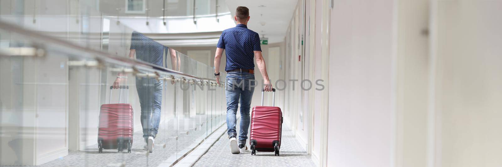 Man with suitcase walking down in hotel corridor back view. Rest in tourist hotel concept