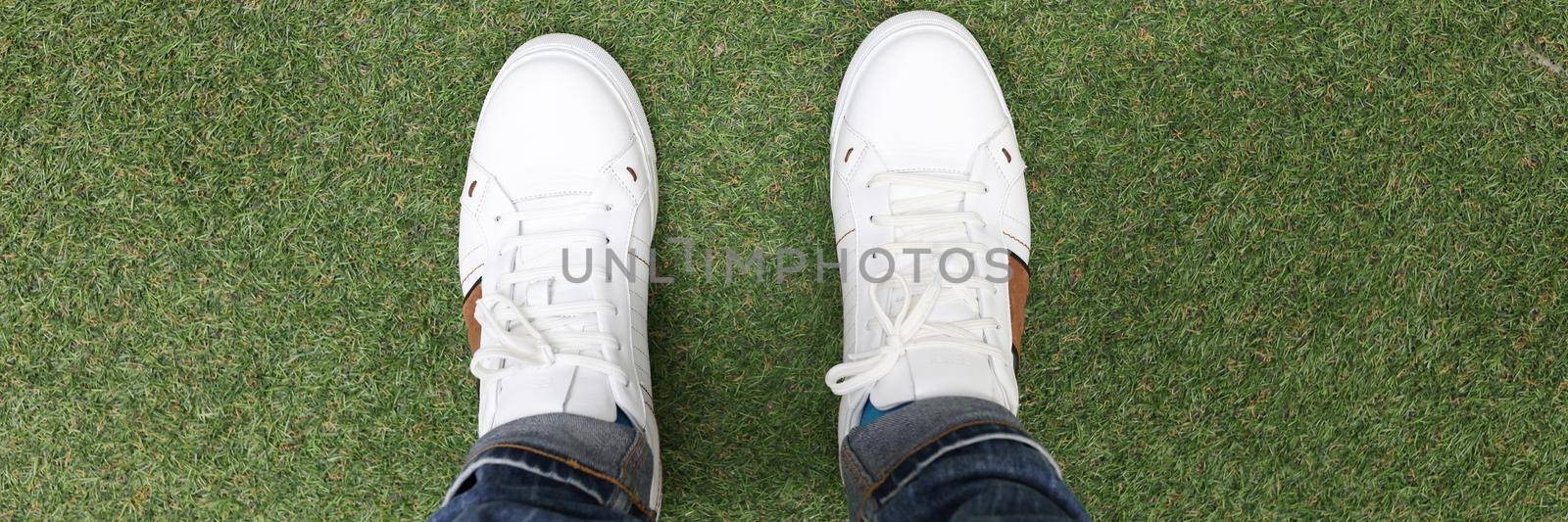 Male feet in white sneakers standing on green grass closeup by kuprevich