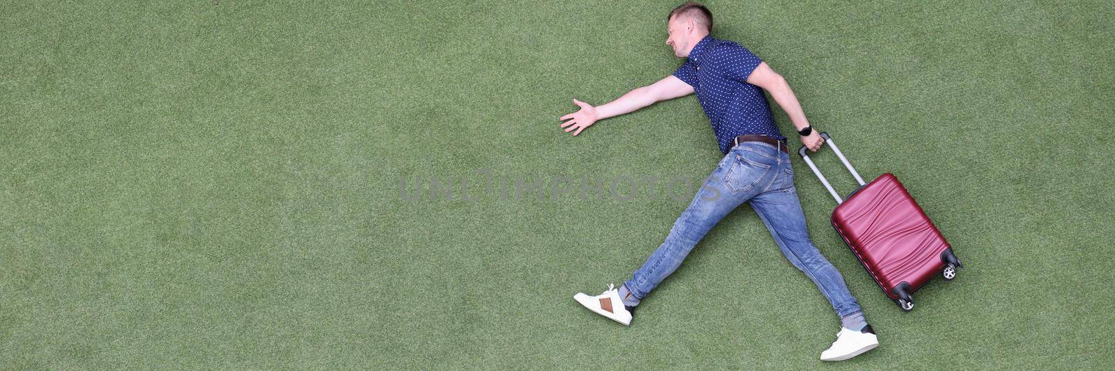 Young man with suitcase walking on green grass top view by kuprevich