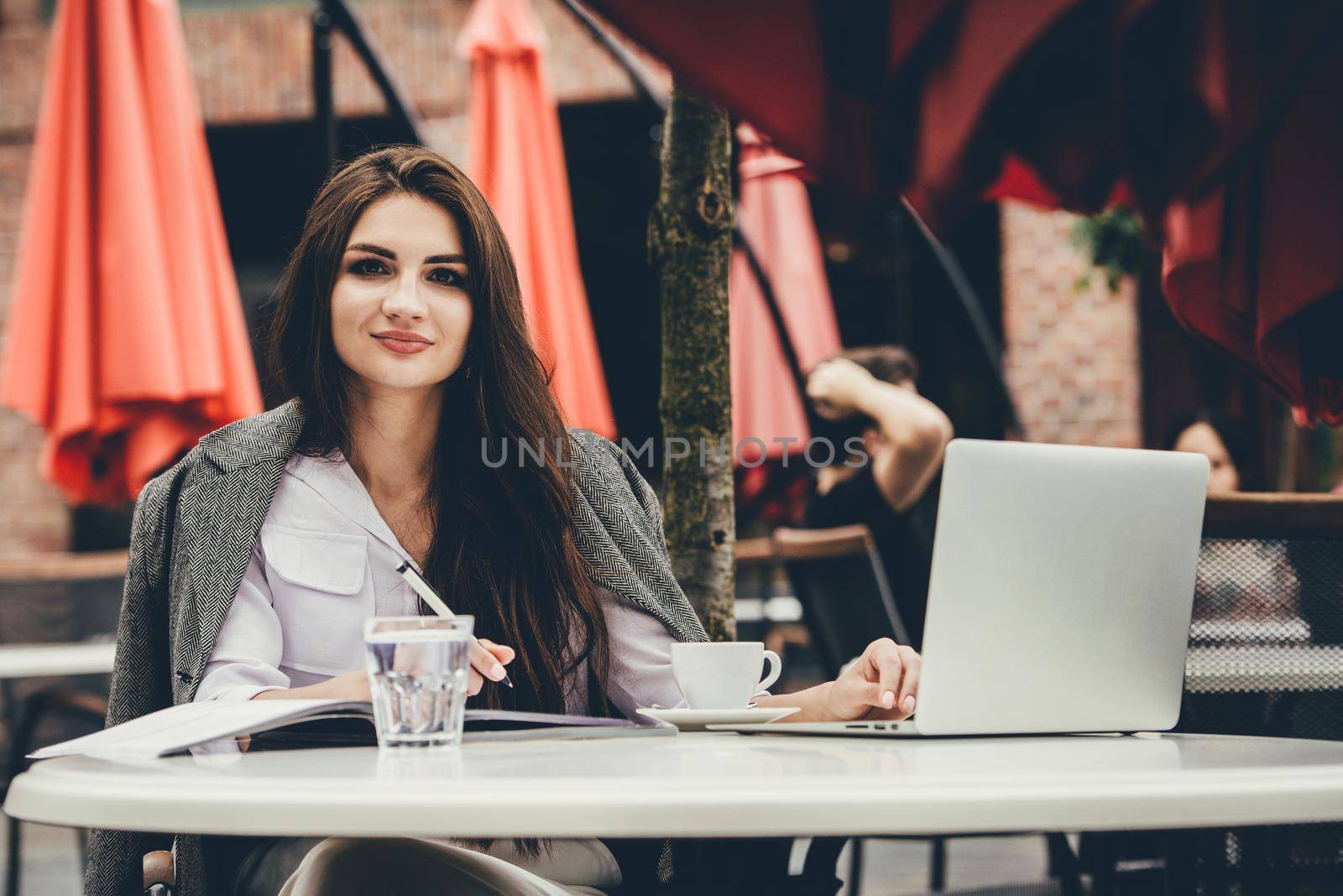 Young freelancer woman using laptop computer sitting at cafe table. Smiling woman working online or studying and learning while using notebook. by Ashtray25