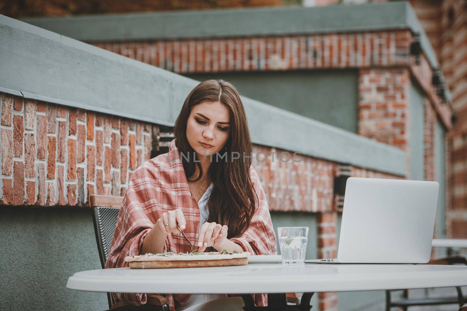 Young freelancer woman using laptop computer and eat pizza while sitting at cafe table. by Ashtray25