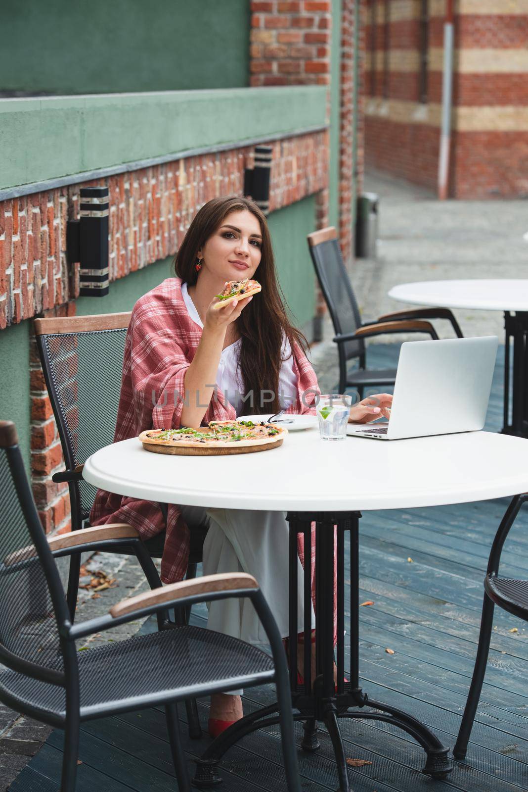 Young freelancer woman using laptop computer and eat pizza while sitting at cafe table. Business People Concept