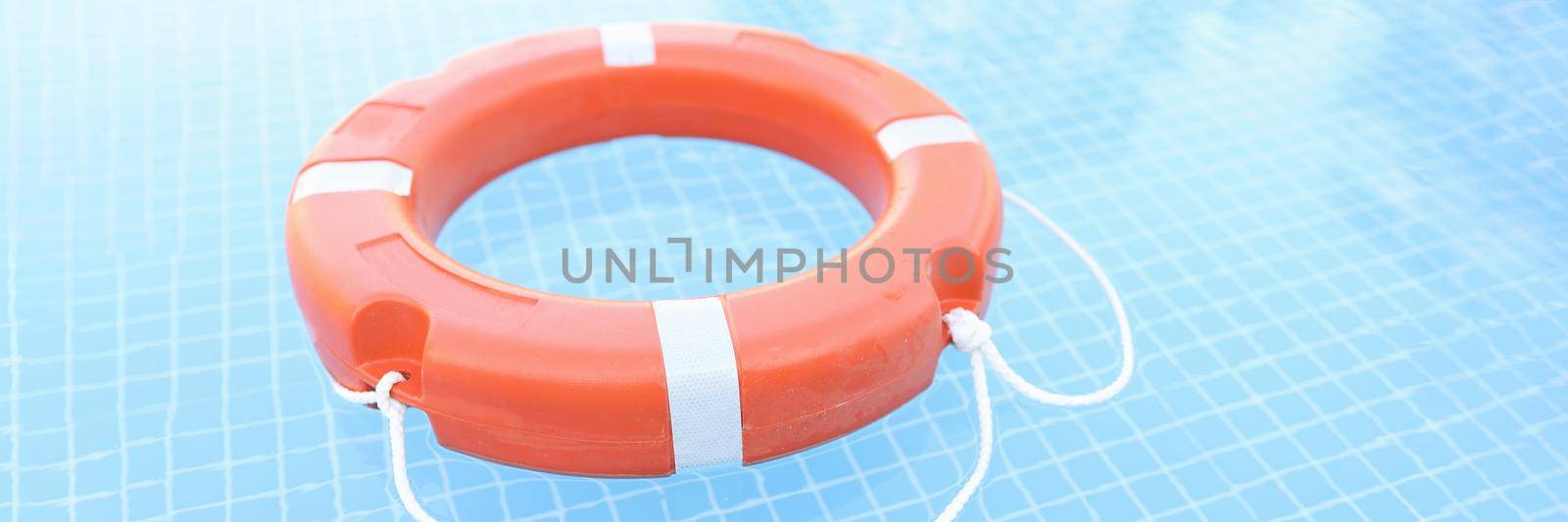 Orange plastic lifebuoy floating in pool closeup. Safety on water concept