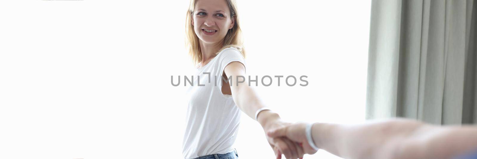 Young woman holding man hand near window at home. Romantic relationship concept