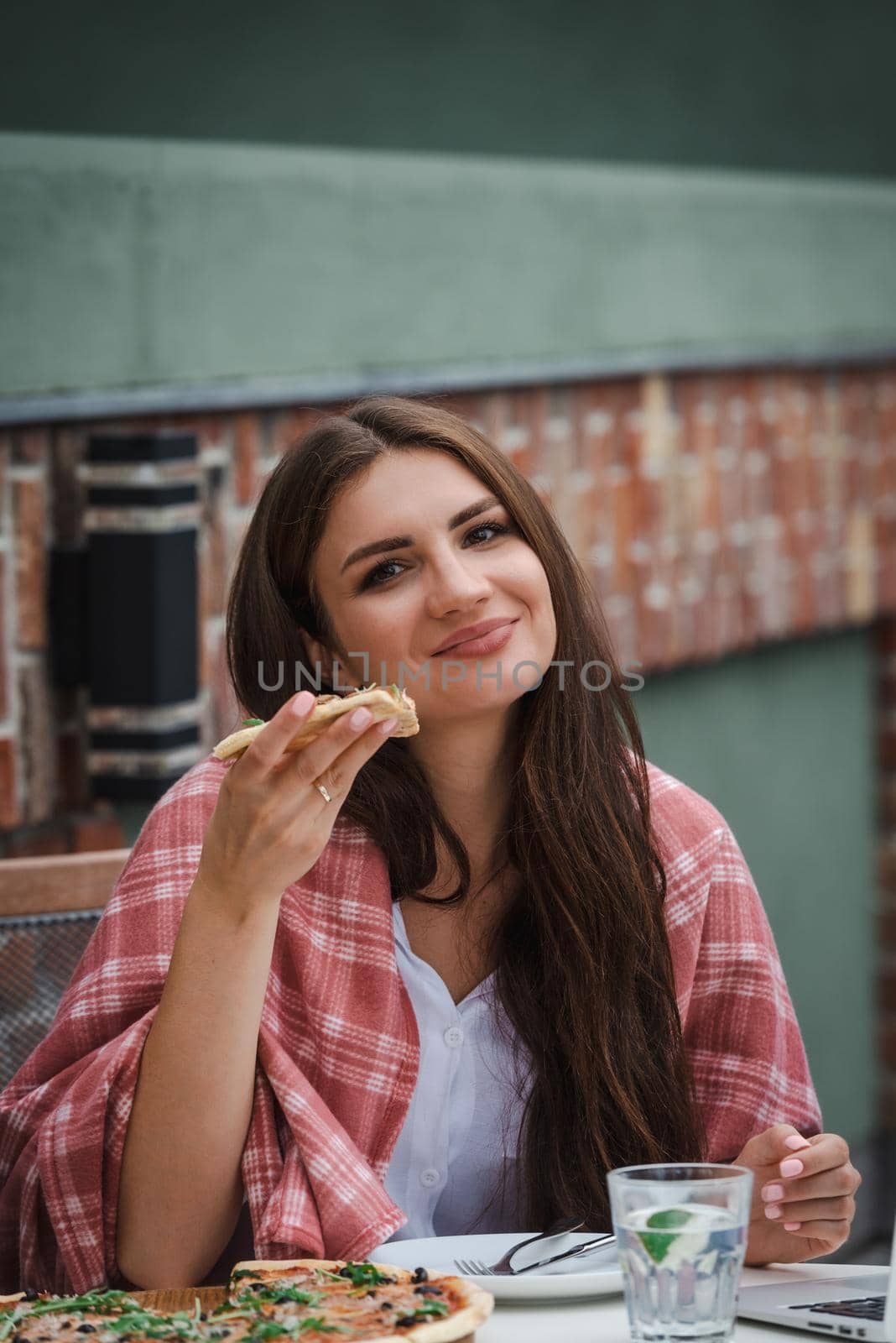 Beautiful brunette girl in a white blouse eating pizza at restaurant. Outdoors