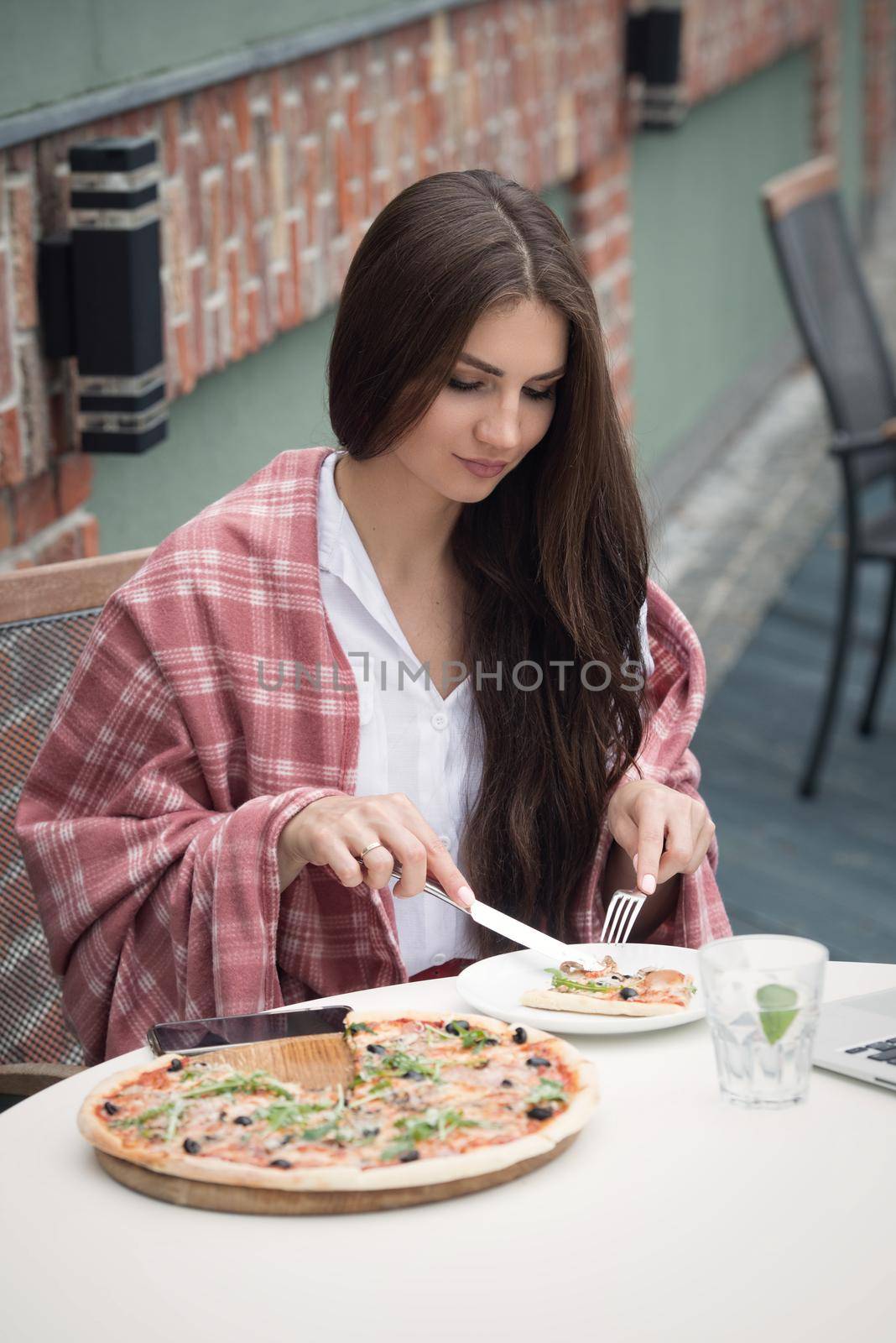 Beautiful brunette girl in a white blouse eating pizza at restaurant. Outdoors