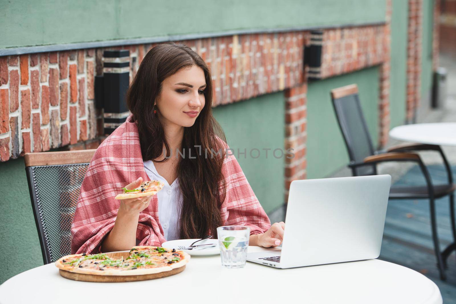 Young freelancer woman using laptop computer and eat pizza while sitting at cafe table. Business People Concept