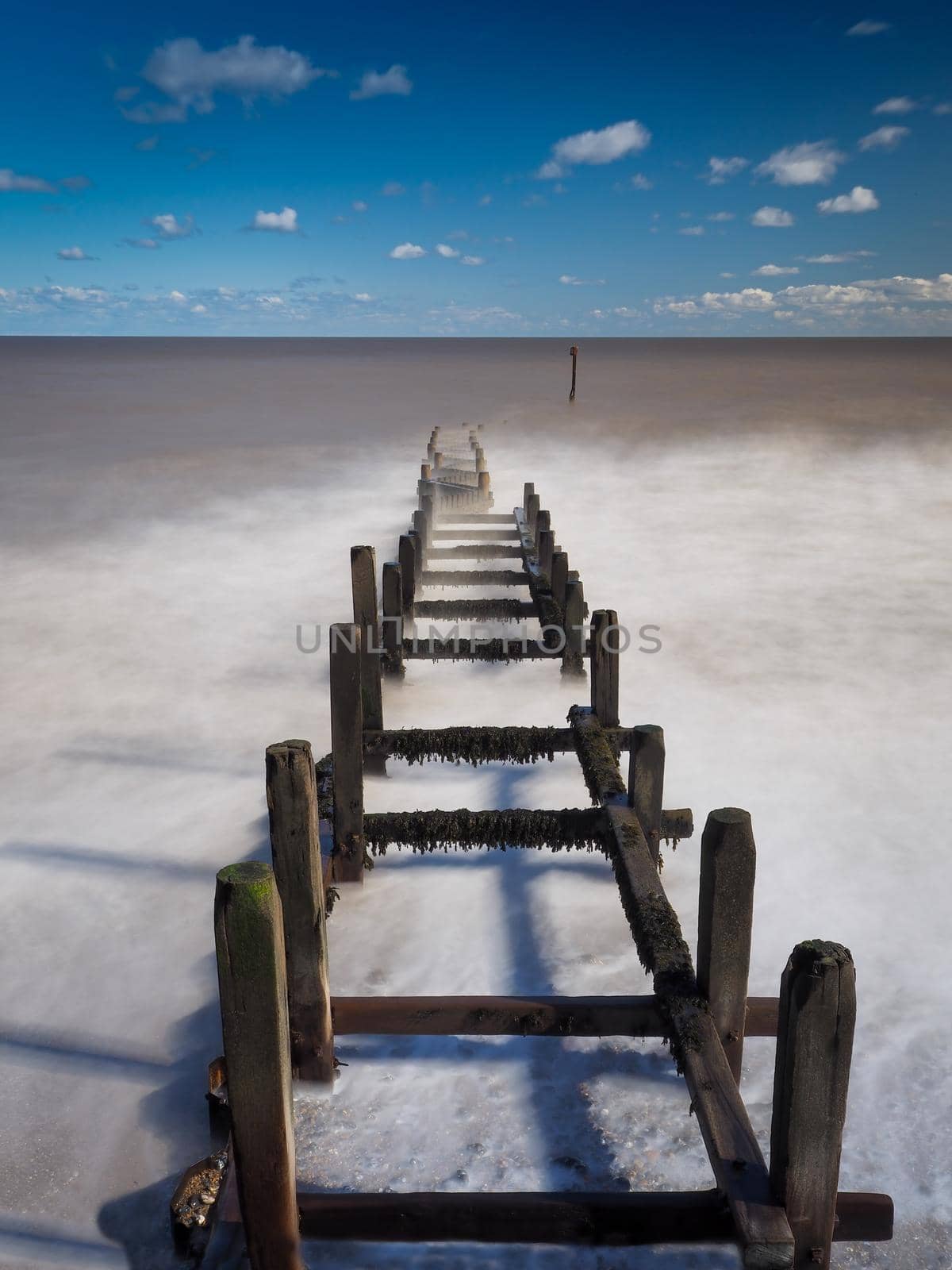 Long exposure image of waves rolling over an interesting wooden groyne stretching out to sea, Overstrand Beach, Norfolk, UK