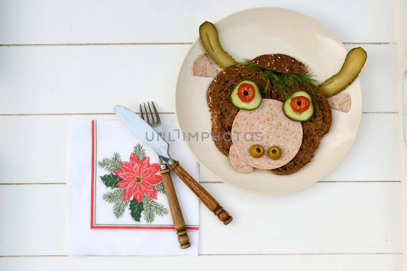 Sandwich in the form of a portrait of a cheerful bull made of dark bread, sausages and vegetables on a plate, on a white wooden background, copispice. High quality photo