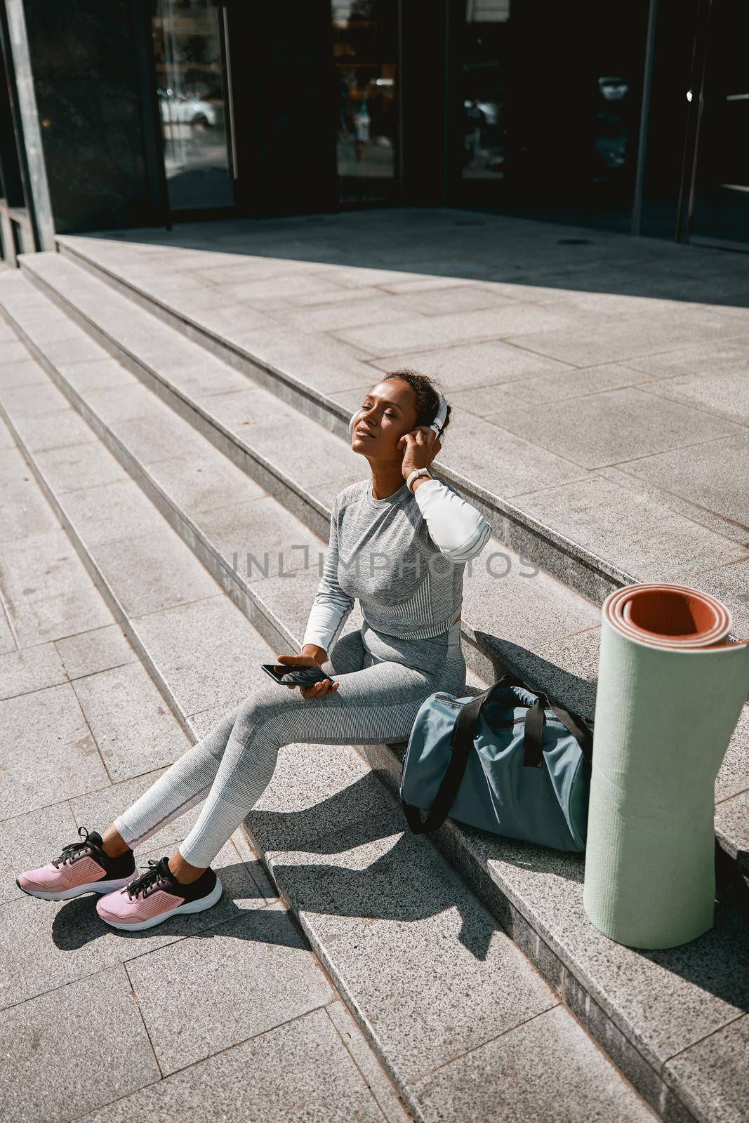 Woman in light gray sportswear sitting outdoors with eyes closed by Yaroslav_astakhov