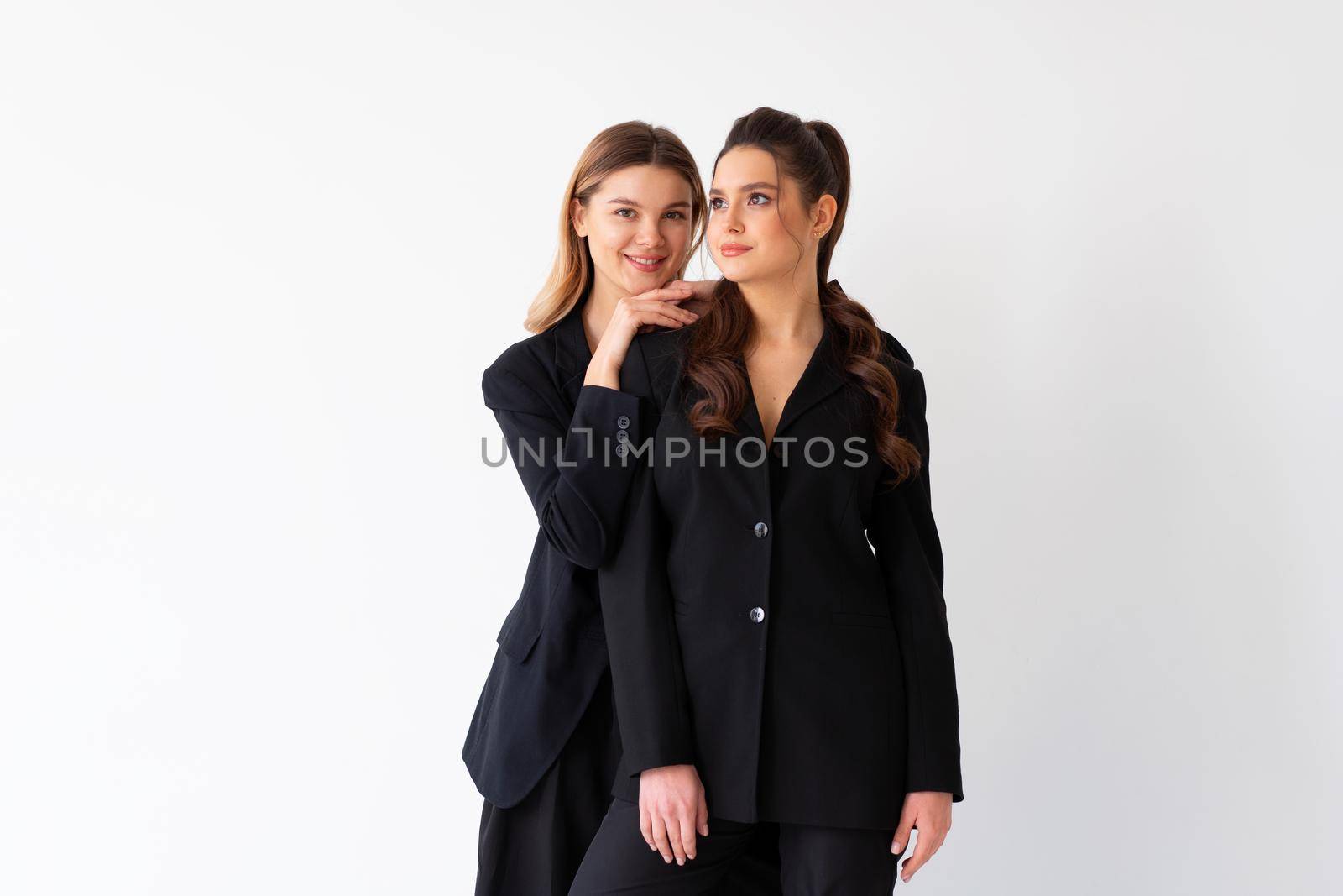 Concept of partnership in business. Two Young businesswoman dressed black formal suit standing studio isolated white background.Blonde woman put her hands on the shoulders of her friend. Smile