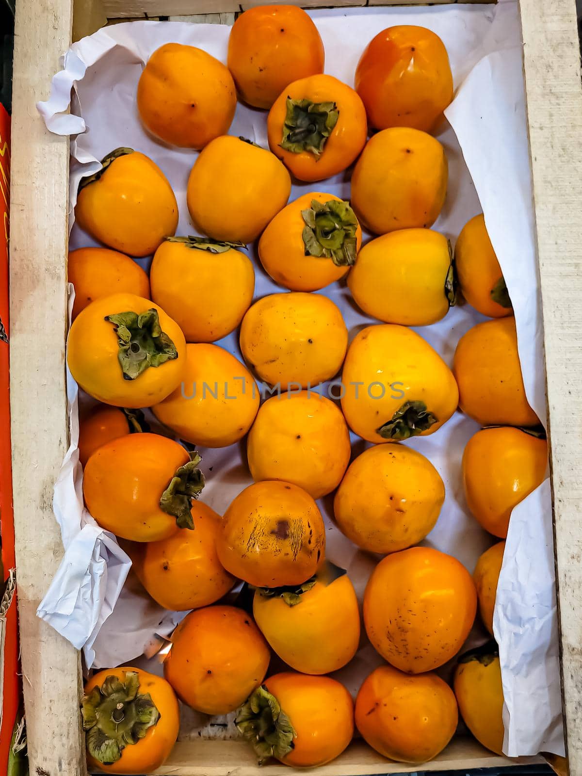Fresh persimmon fruits are in a box in the store by Milanchikov